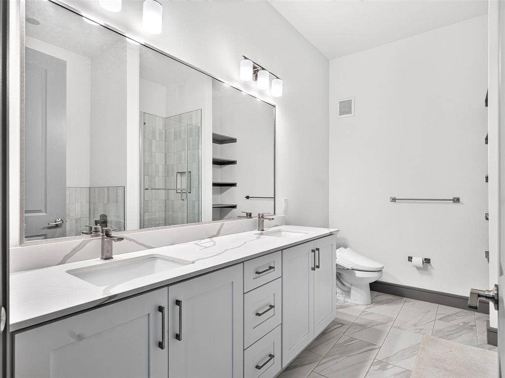 2700 Old Denton Road, #2212, Carrollton, TX 75007 Dual vanity with integrated sinks, expansive mirror, light-toned tile flooring, contemporary light fixtures, and a shower enclosure visible in reflection