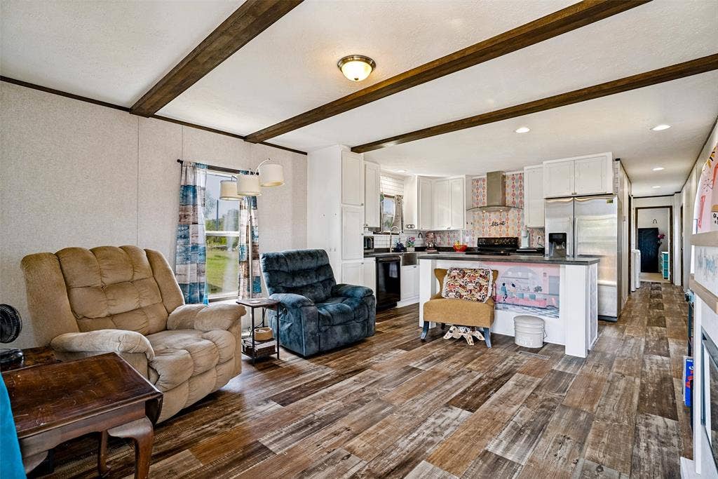 4415 Woodland Drive, Granbury, TX 76048 Open-concept living area with wood-finish flooring, exposed ceiling beams, a kitchen featuring white cabinetry, and stainless-steel appliances