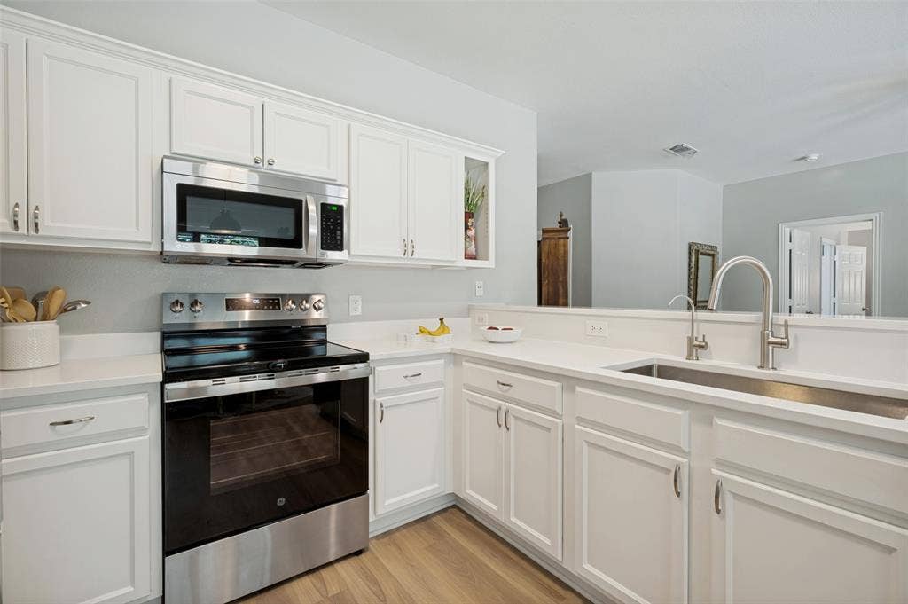3707 Redwood Circle, Melissa, TX 75454 Contemporary kitchen featuring white cabinetry with brushed nickel hardware, stainless steel appliances including a built-in wall oven and microwave, quartz countertops, and a spacious island with an undermount sink and chrome pull-down faucet