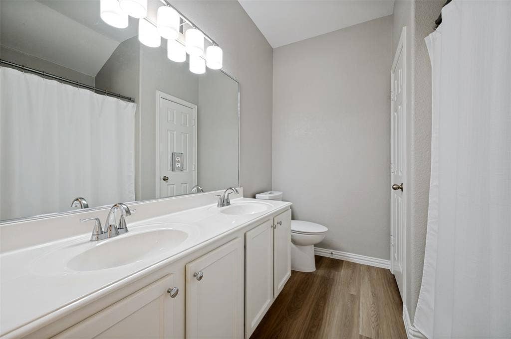 3707 Redwood Circle, Melissa, TX 75454 Double vanity with chrome fixtures and integrated sinks, wood-finish flooring, and a large wall-mounted mirror