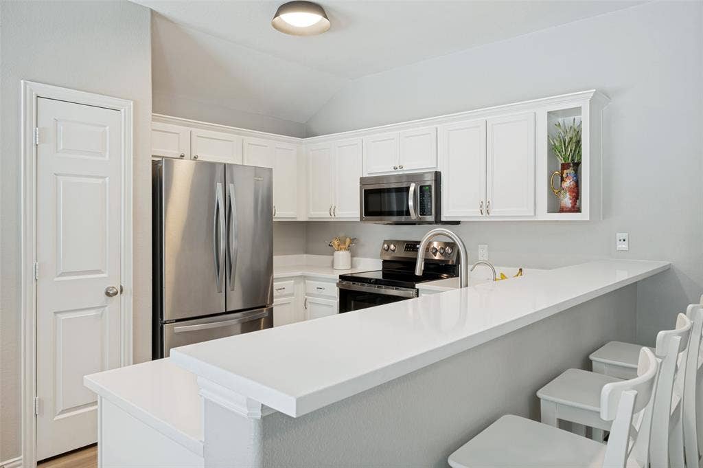 3707 Redwood Circle, Melissa, TX 75454 White shaker cabinetry, stainless steel appliances, white countertops, built-in microwave, and a breakfast bar