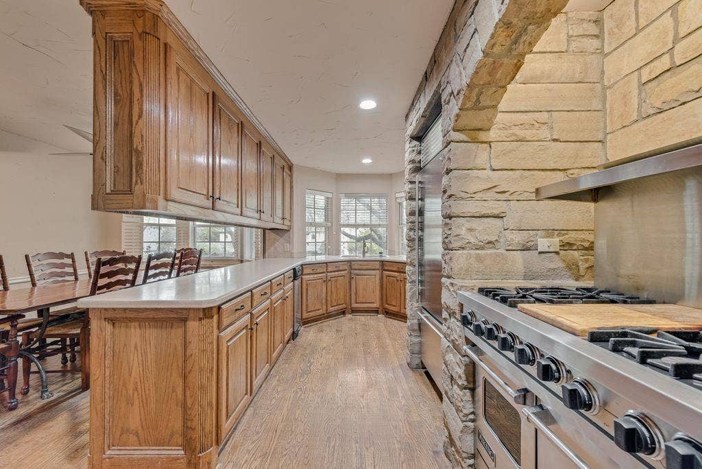 2 Eastshore Road, Heath, TX 75032 Stone archway with built-in range, stainless steel appliances, extensive wood cabinetry, light-toned countertops, and wood-finish flooring