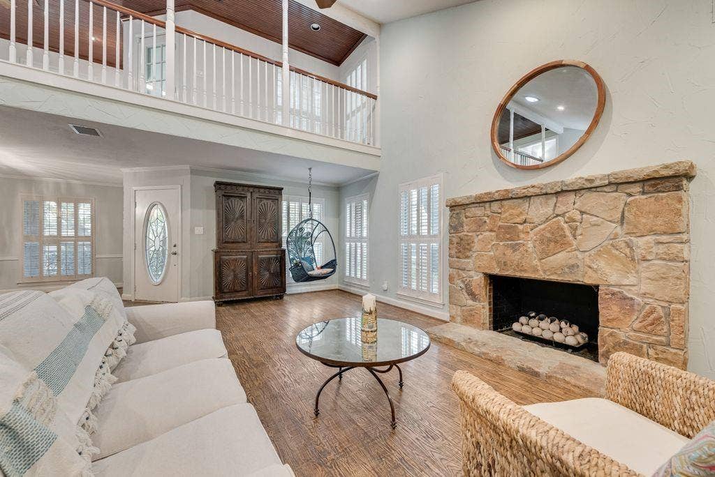 2 Eastshore Road, Heath, TX 75032 Stone-faced fireplace with hearth, wood-finish flooring, white plantation shutters, and an upper-level balcony with white balusters