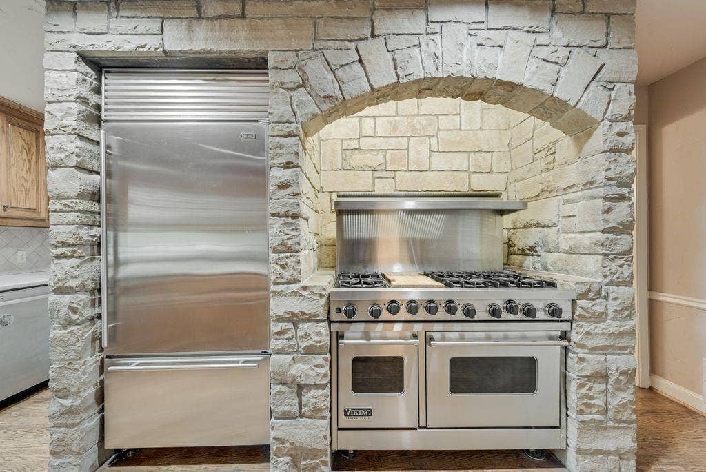 2 Eastshore Road, Heath, TX 75032 Integrated stainless steel refrigerator, stone archway, stainless steel range with multiple burners, integrated stainless steel oven, and stone wall cladding