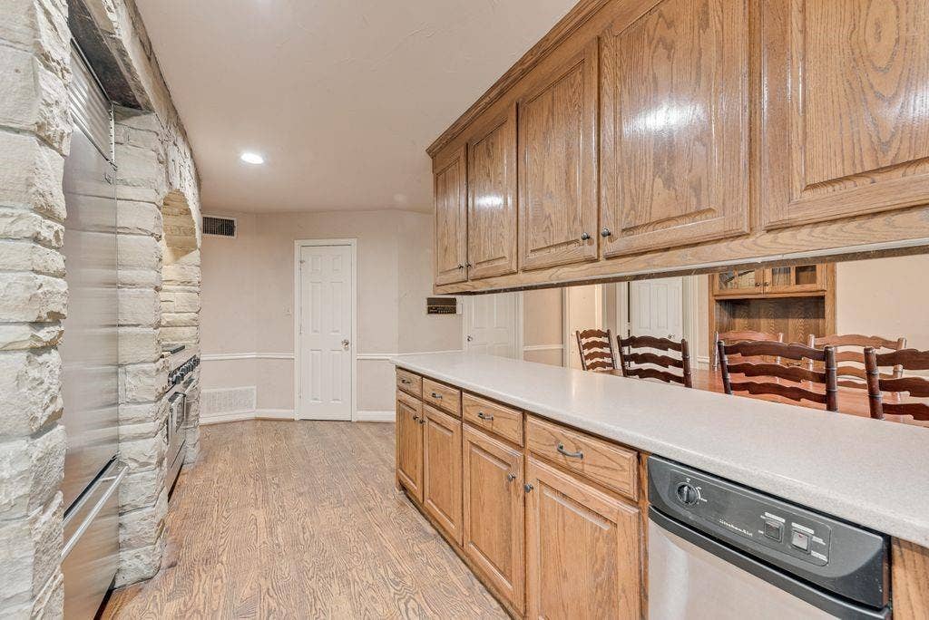2 Eastshore Road, Heath, TX 75032 Wood-finish flooring, stone-clad archway, oak cabinetry, light-toned countertops, and a built-in stainless steel dishwasher