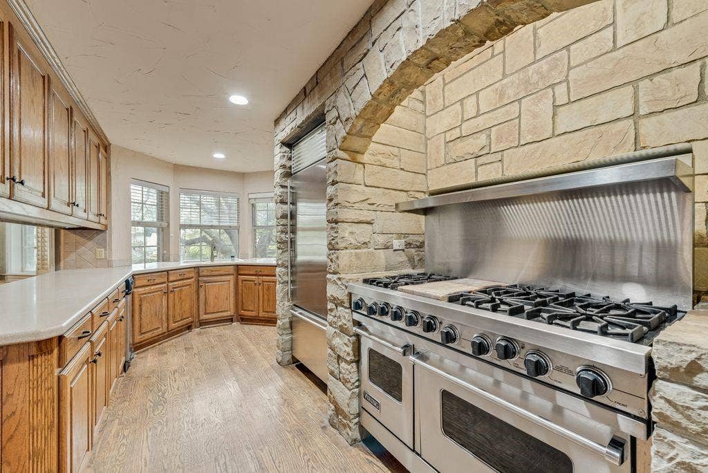 2 Eastshore Road, Heath, TX 75032 Gourmet kitchen featuring a stainless steel range with griddle, stone archway, built-in stainless steel refrigerator, wood-finish flooring, and ample cabinetry