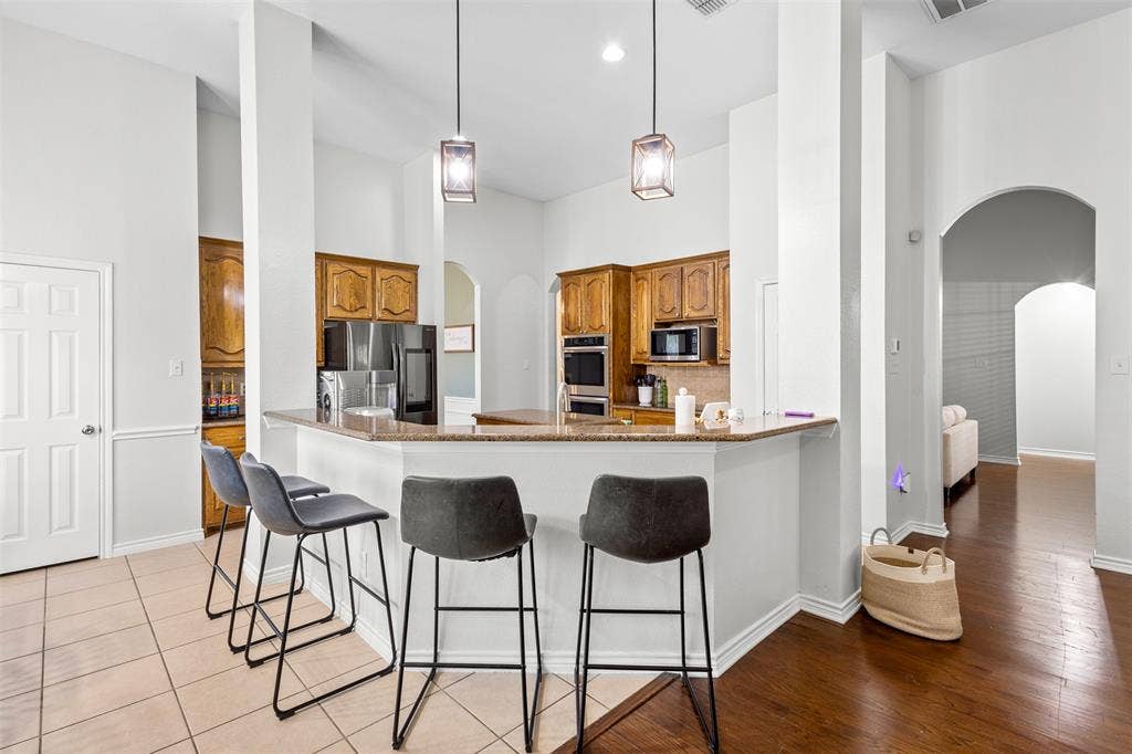 5413 Compassion Drive, Midlothian, TX 76065 Kitchen featuring wood cabinetry, built-in stainless steel appliances, a breakfast bar with a granite-style countertop, and pendant lighting