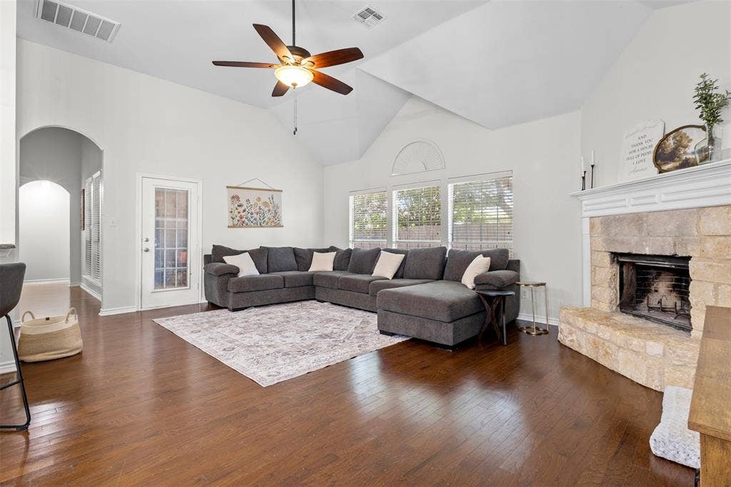 5413 Compassion Drive, Midlothian, TX 76065 Living area featuring vaulted ceilings, wood-finish flooring, a stone-faced fireplace with a mantel, a ceiling fan, and large windows