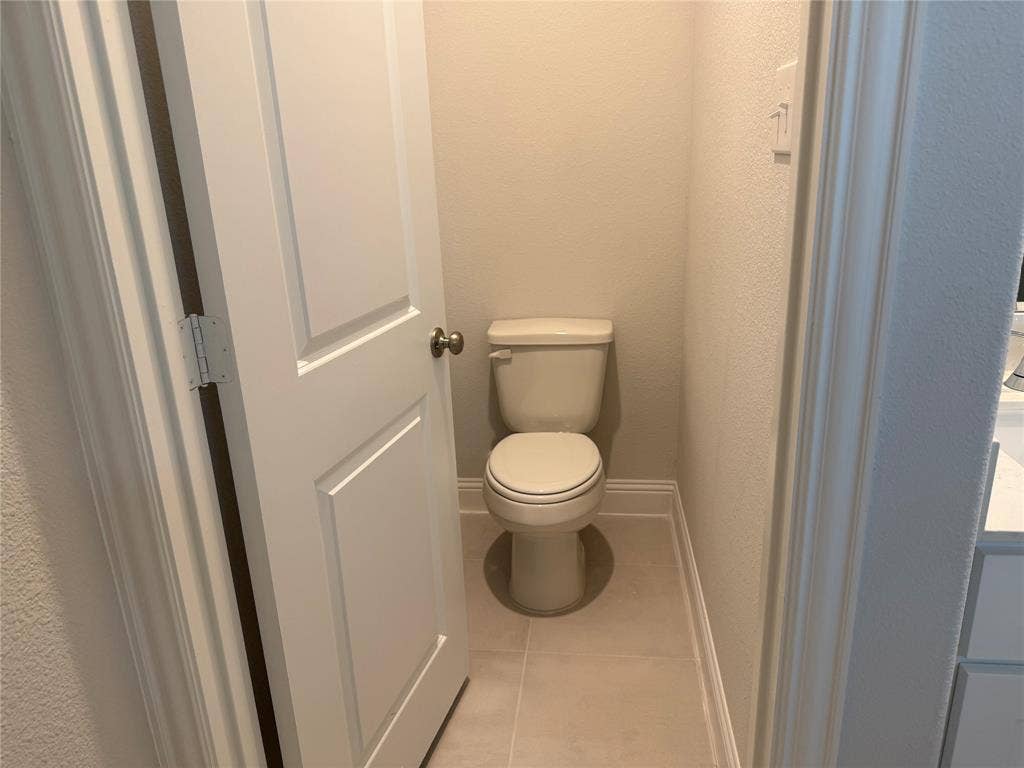 Modern toilet with a light-colored tile floor, light-toned walls, and white trim molding
