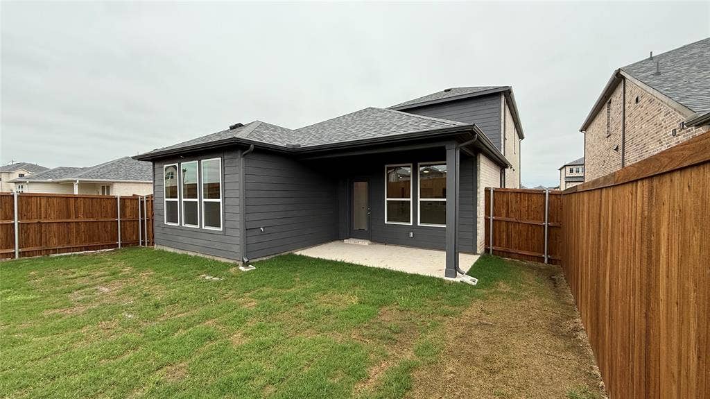 Private fenced yard with a covered patio, featuring a dark gray exterior, white window frames, and a shingle roof