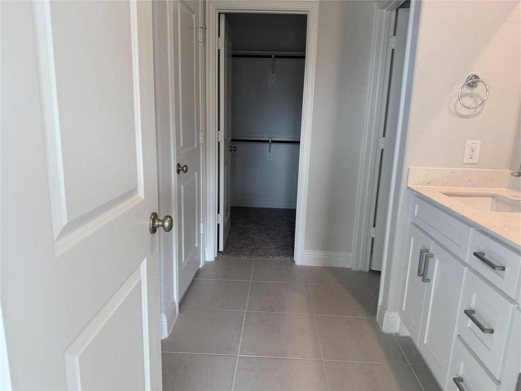 White paneled doors, light gray tile flooring, white vanity with integrated sink, light countertop, and brushed nickel hardware