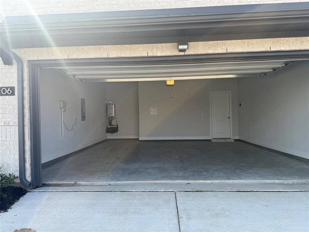 Spacious garage featuring concrete flooring, an interior access door, wall-mounted water heater, and overhead lighting
