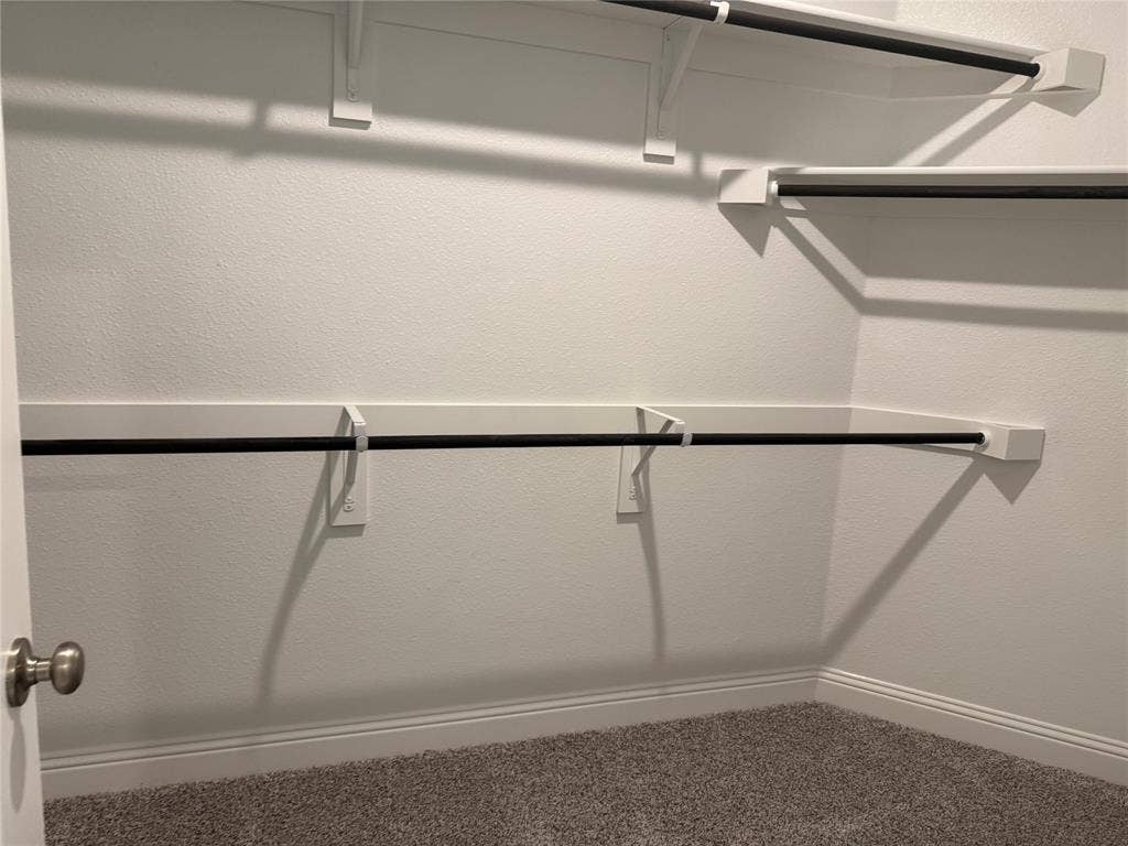Built-in closet shelving system with multiple hanging rods, white wall finishes, and gray carpet flooring