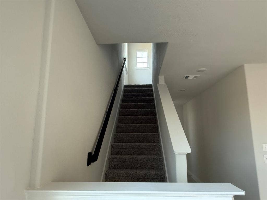 Carpeted staircase with a black handrail and white newel posts