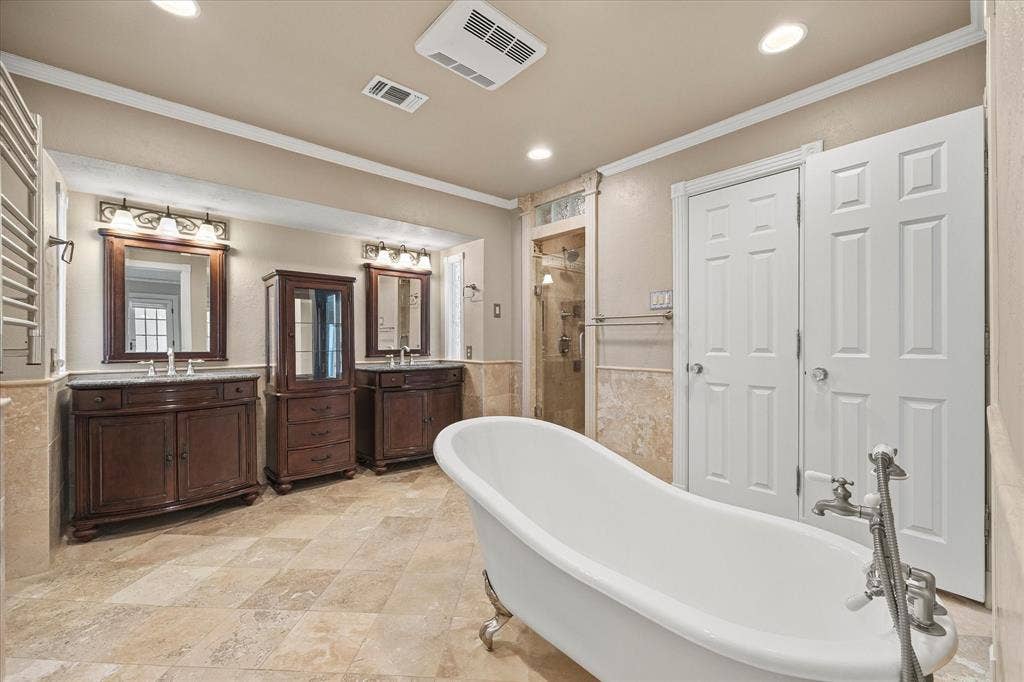 4001 Keele Drive, Garland, TX 75041 Update primary bath featuring a freestanding slipper tub, dual vanities, travertine flooring, and walk-in shower. This spa-type retreat also features two closets on each side.