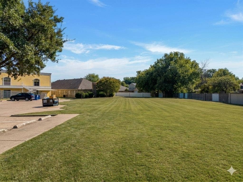 Expansive grass lawn with mature trees and a perimeter fence