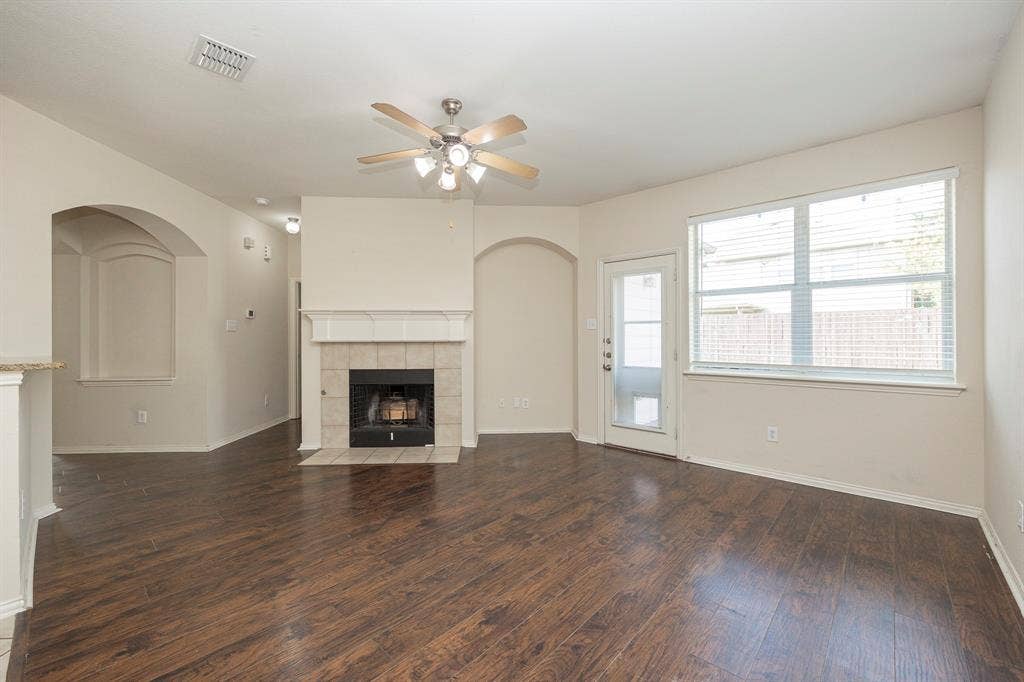 5728 Calloway Drive, McKinney, TX 75070 Wood-finish flooring, fireplace with tile surround, ceiling fan, archway detail, and exterior door