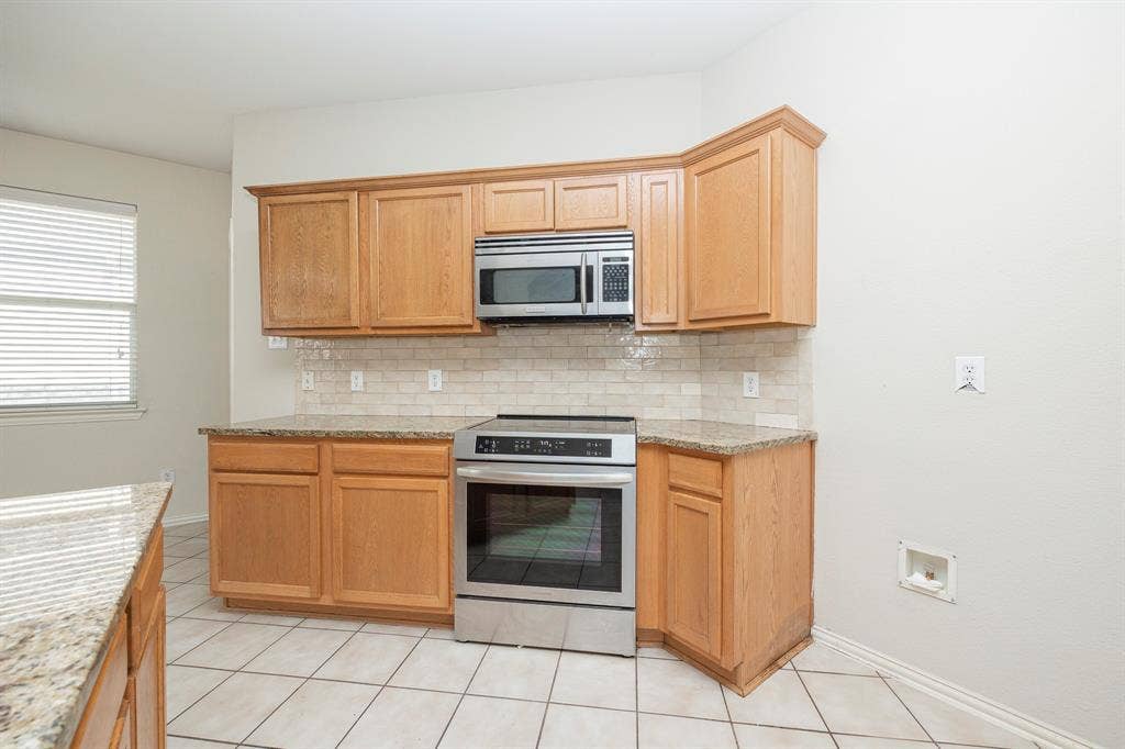 5728 Calloway Drive, McKinney, TX 75070 Kitchen featuring wood cabinetry, stainless steel microwave, stainless steel range, patterned tile backsplash, and light-toned countertops
