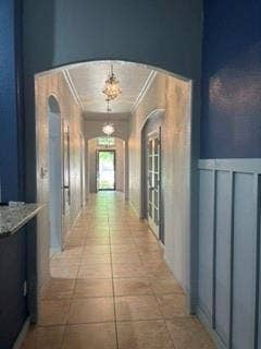 1316 Shelley Drive, Burleson, TX 76028 Arched entryway leading to a long hallway with tile flooring, featuring two chandeliers and a paneled wall detail