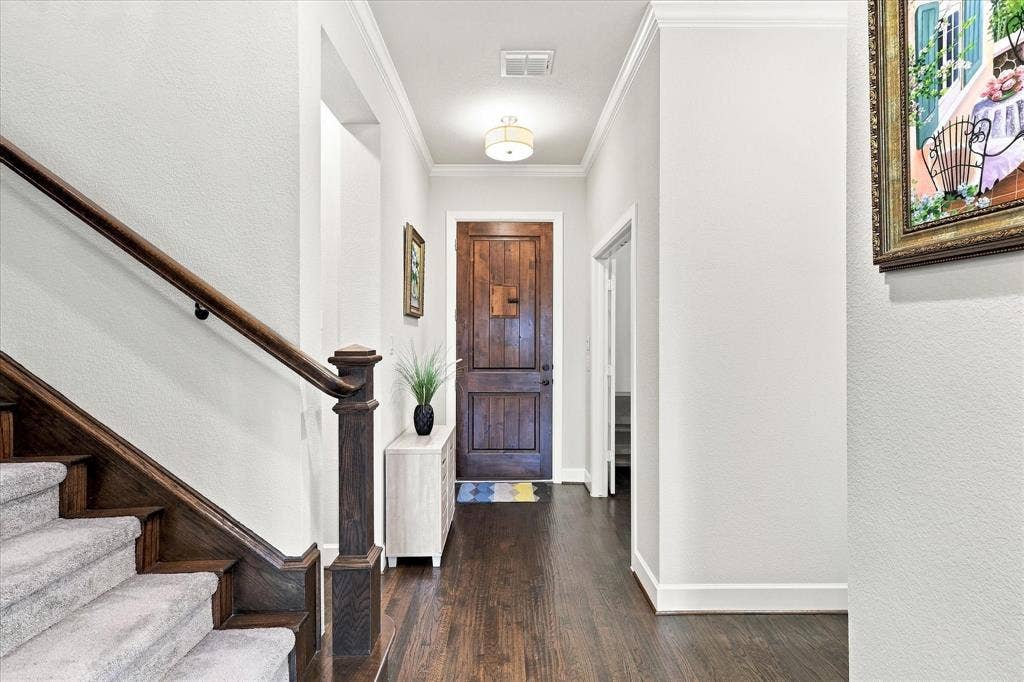 Staircase with wood newel post and handrail, carpeted treads, wood-finish flooring, and crown molding