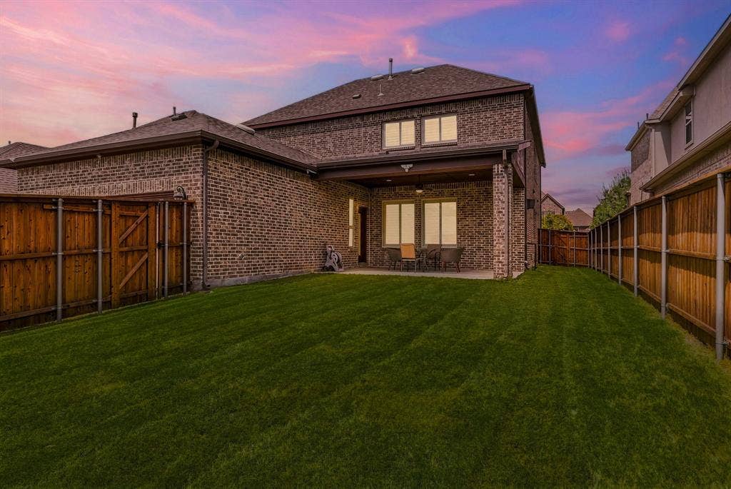 Expansive backyard featuring a manicured lawn, full privacy fencing, and a covered patio