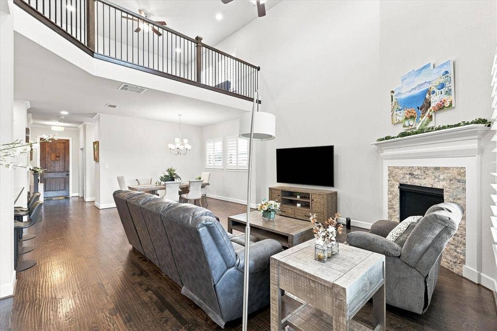 Open-concept living area featuring soaring ceilings with an upper-level mezzanine, hardwood flooring throughout, and a wall-mounted flat-screen television