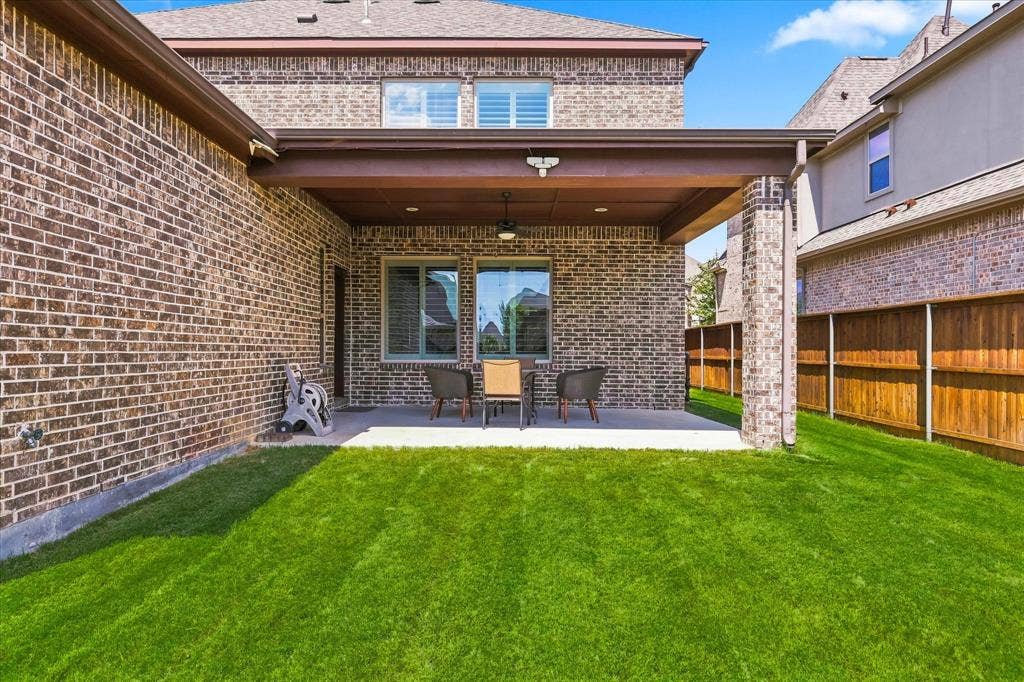 Expansive backyard retreat featuring a pristine maize lawn, brick-and-stone exterior with covered patio, large multi-pane glass doors, recessed lighting, and wooden garage doors visible to the side