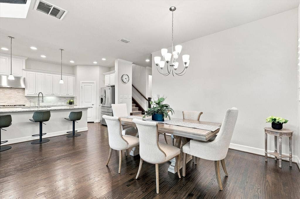 Wood-finish flooring throughout, complemented by a kitchen featuring white cabinetry, pendant lighting, stainless steel appliances, and a tile backsplash