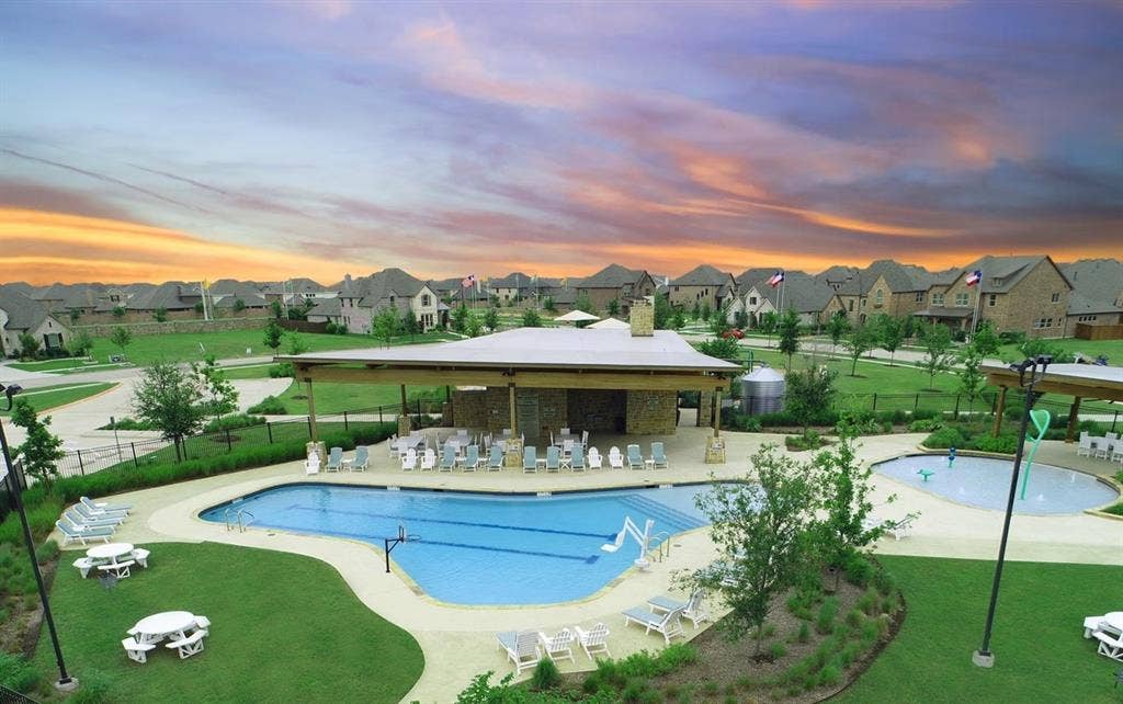 Expansive community pool with multiple entry points, an adjacent splash pad, and a covered pavilion featuring a stone-clad structure