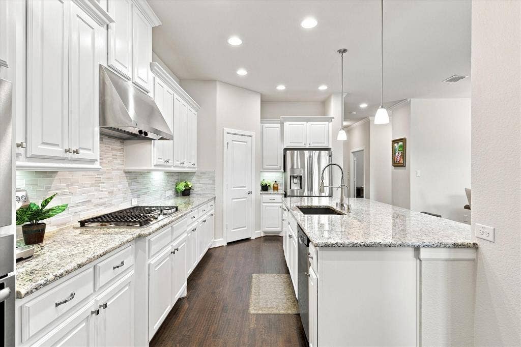 White cabinetry, stainless steel appliances, granite countertops, wood-finish flooring, and recessed lighting