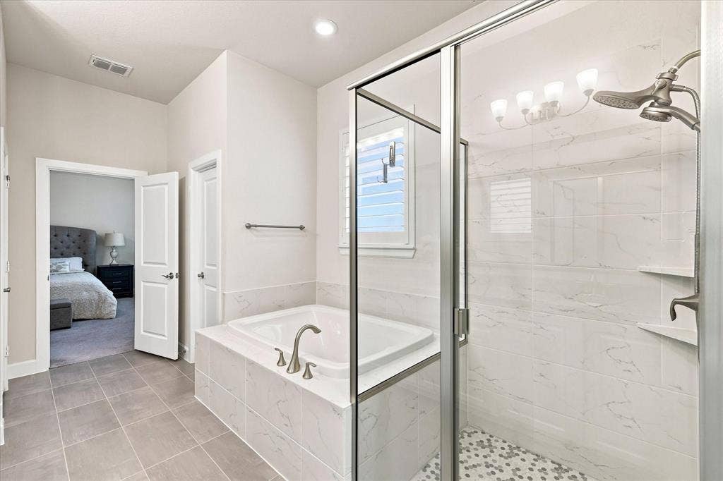 Spa-inspired primary bathroom featuring a freestanding soaking tub with chrome fixtures, a walk-in shower enclosure with glass panels and rainfall showerhead, marble-look tile walls, pebble tile accents, and recessed lighting