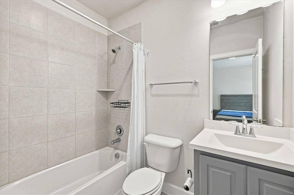 Bathtub with tiled surround, shower fixture, white toilet, vanity with integrated sink, and cabinet storage