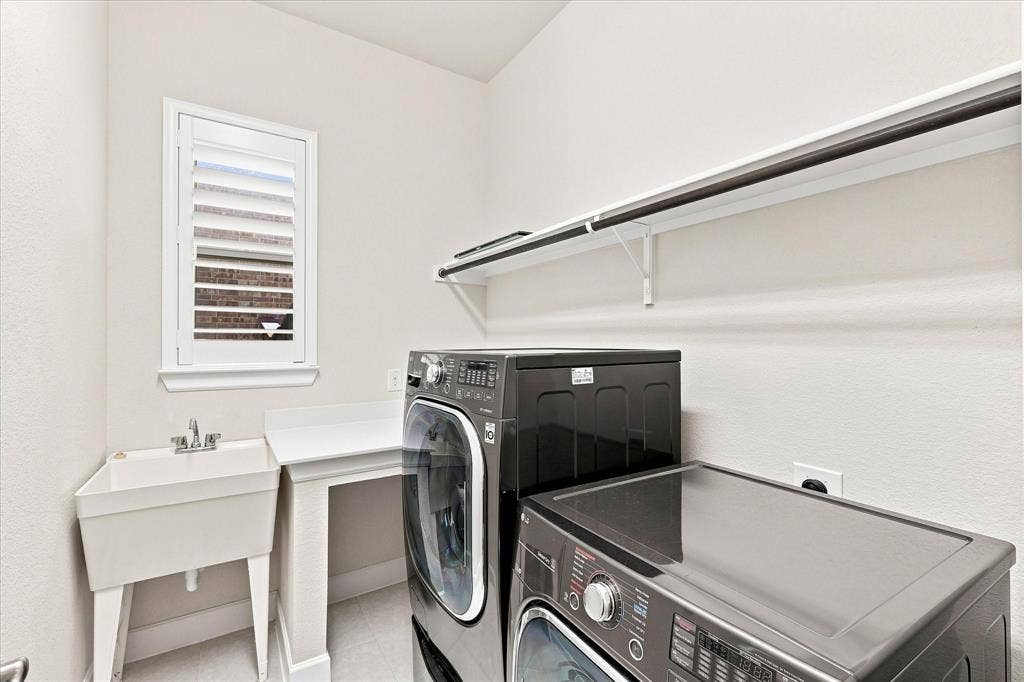 Utility room featuring a window with white louvered shutters, a utility sink, a built-in countertop, and an overhead shelving unit with a hanging rod