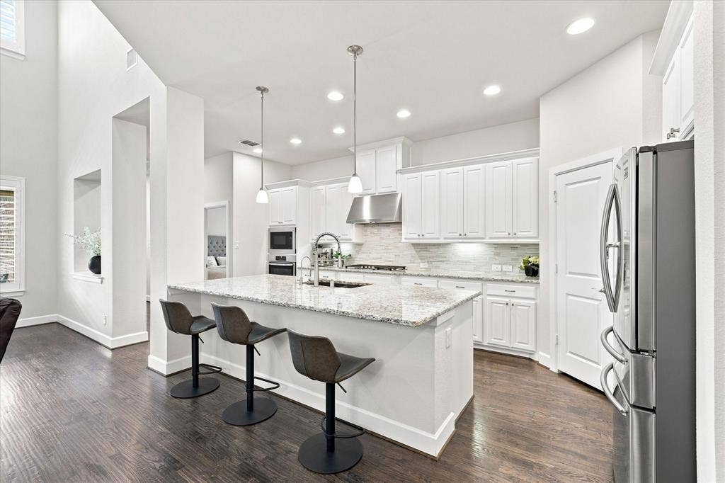 Kitchen featuring white cabinetry, granite countertops, stainless steel appliances, and wood-finish flooring