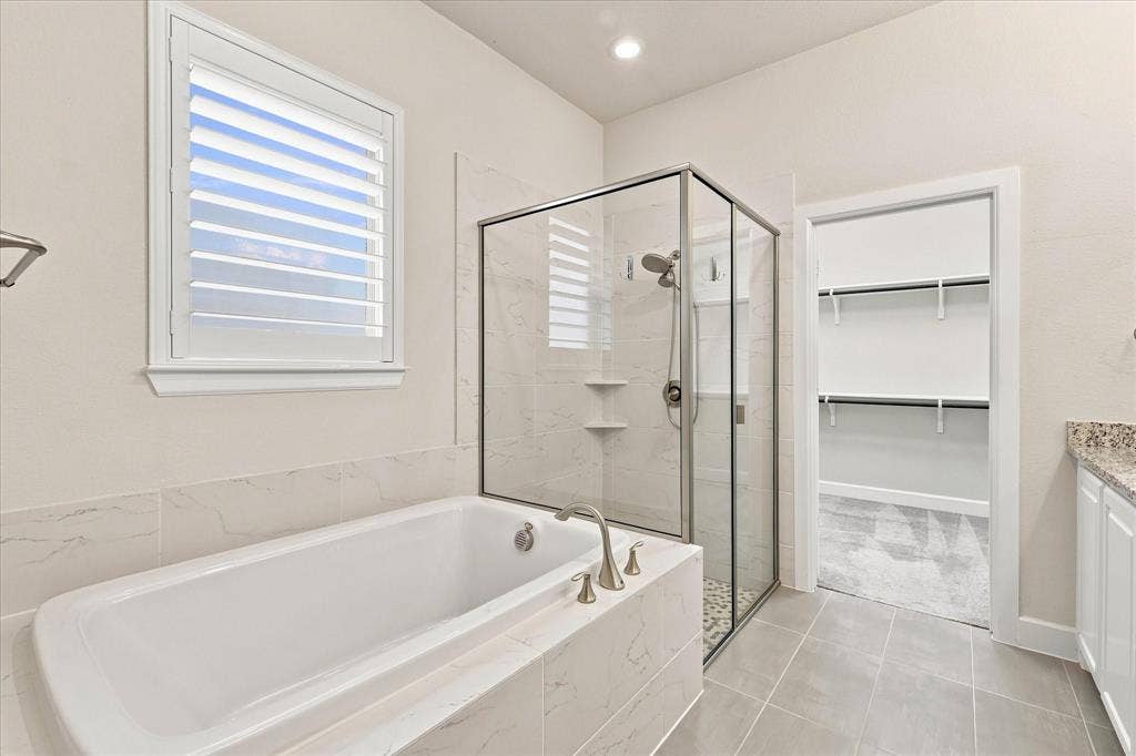 Soaking tub with brushed nickel fixtures, glass-enclosed shower with tile surround, and tile flooring