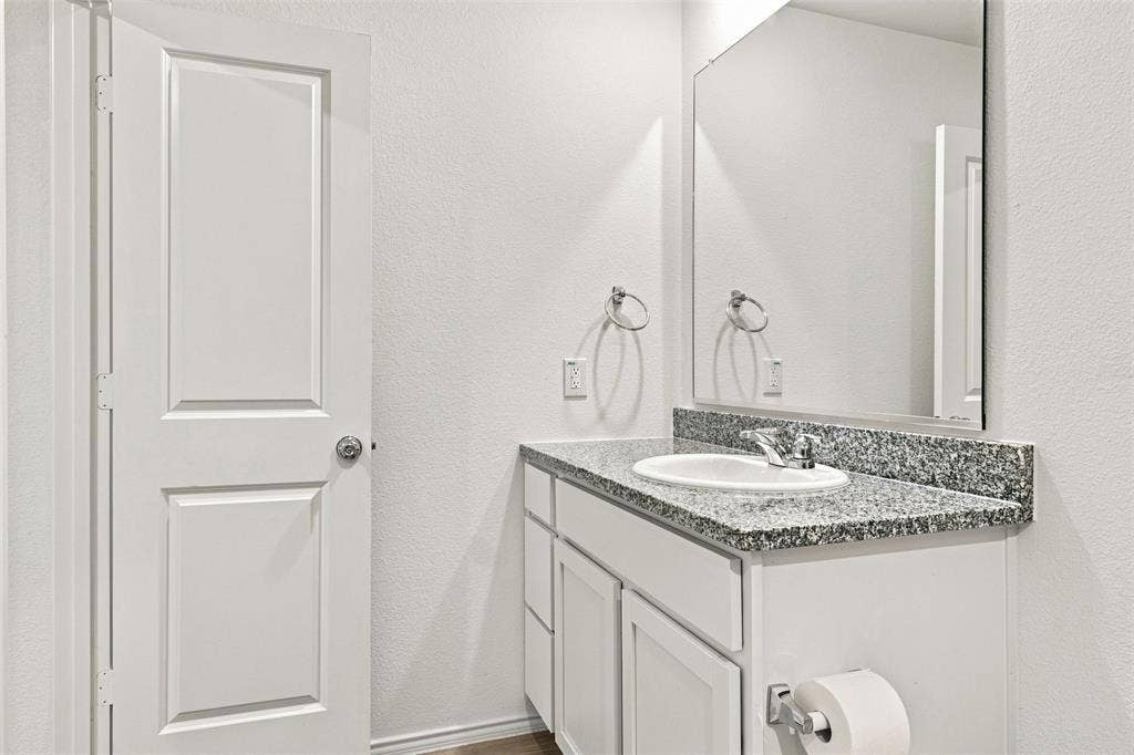 3409 Flicker Lane, McKinney, TX 75071 Vanity with an integrated sink, granite countertop, chrome faucet, and storage cabinetry
