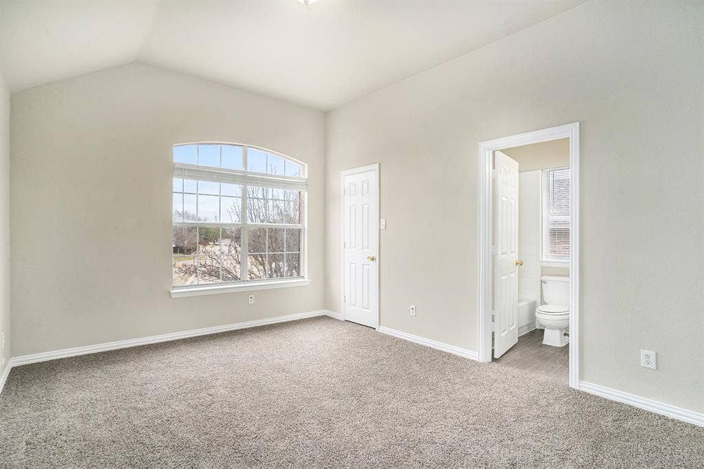 Unfurnished bedroom with carpet, lofted ceiling, and ensuite bathroom