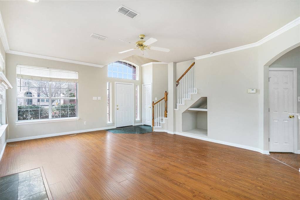 Unfurnished living room featuring crown molding, built in shelves, wood-type flooring, and ceiling fan