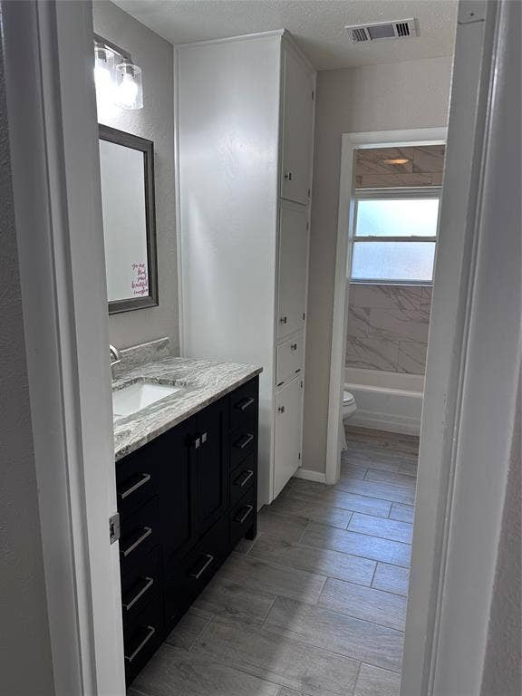 1321 Hurstview Drive, Hurst, TX 76053 Bathroom featuring a dark vanity with a light-colored countertop, built-in storage cabinetry, and wood-finish tile flooring