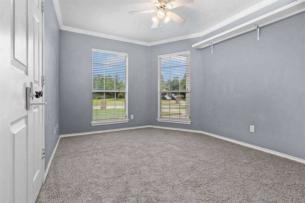 833 Greenwood Circle, Lindale, TX 75771 Bright corner bedroom with dual windows framing outdoor scenery, neutral gray walls, neutral carpet flooring, and ceiling fan with integrated lighting