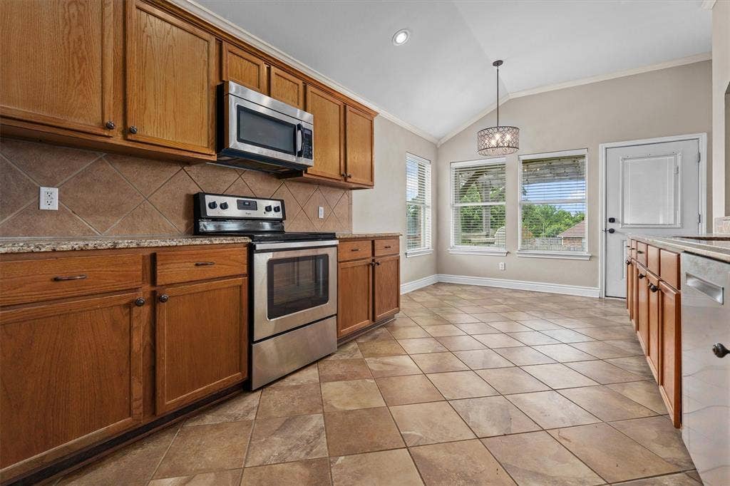 833 Greenwood Circle, Lindale, TX 75771 Galley-style kitchen featuring stainless steel appliances, wood cabinetry with bronze hardware, granite countertops, and diagonal tile flooring