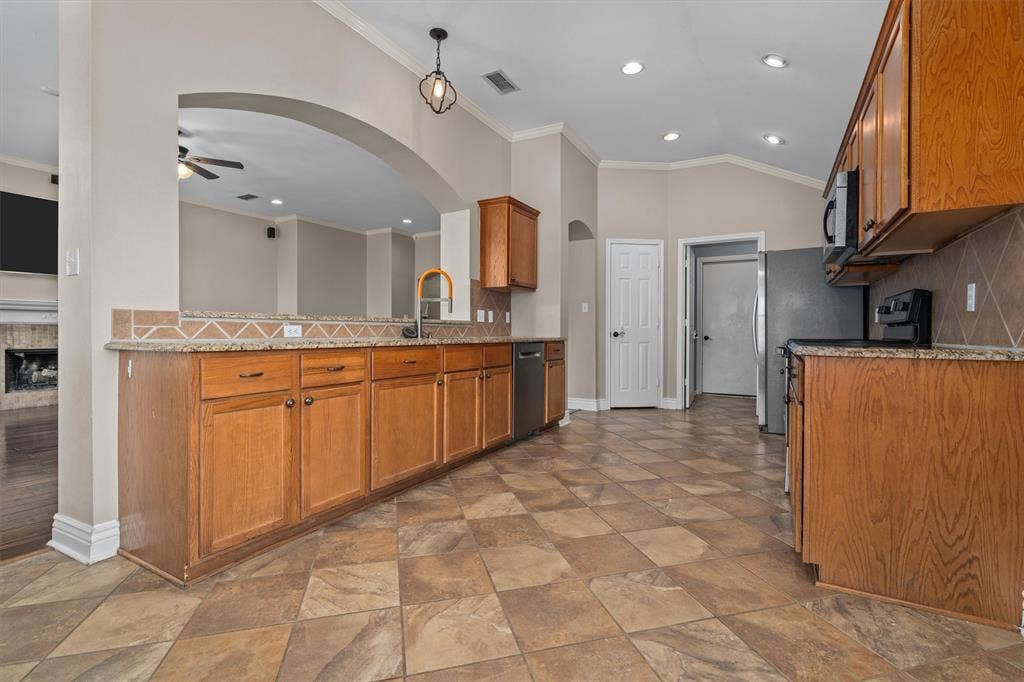 833 Greenwood Circle, Lindale, TX 75771 Spacious kitchen and dining area showcasing rich wood cabinetry, dual sink vanity with decorative backsplash, stainless steel appliances, recessed ceiling lighting, and diagonal tile flooring throughout the open layout