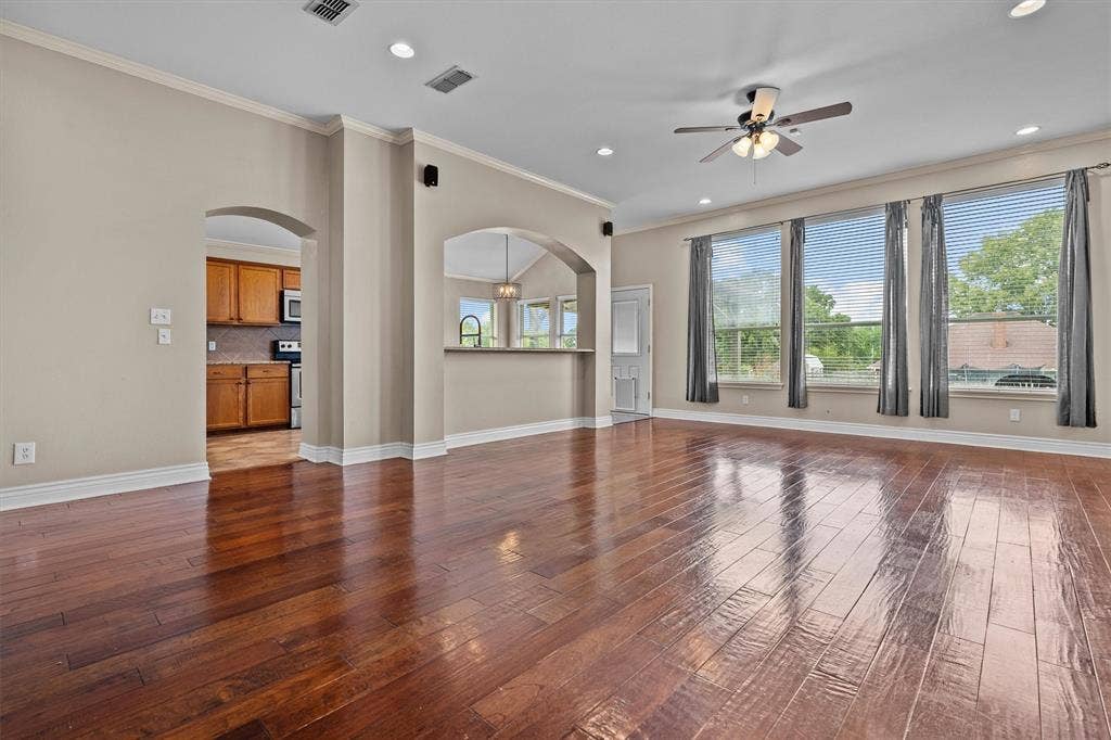 833 Greenwood Circle, Lindale, TX 75771 Expansive open-concept living area showcasing rich wood-finish flooring throughout, soaring ceilings with recessed lighting and ceiling fan, and abundant natural light from multiple large multi-pane glass doors and windows