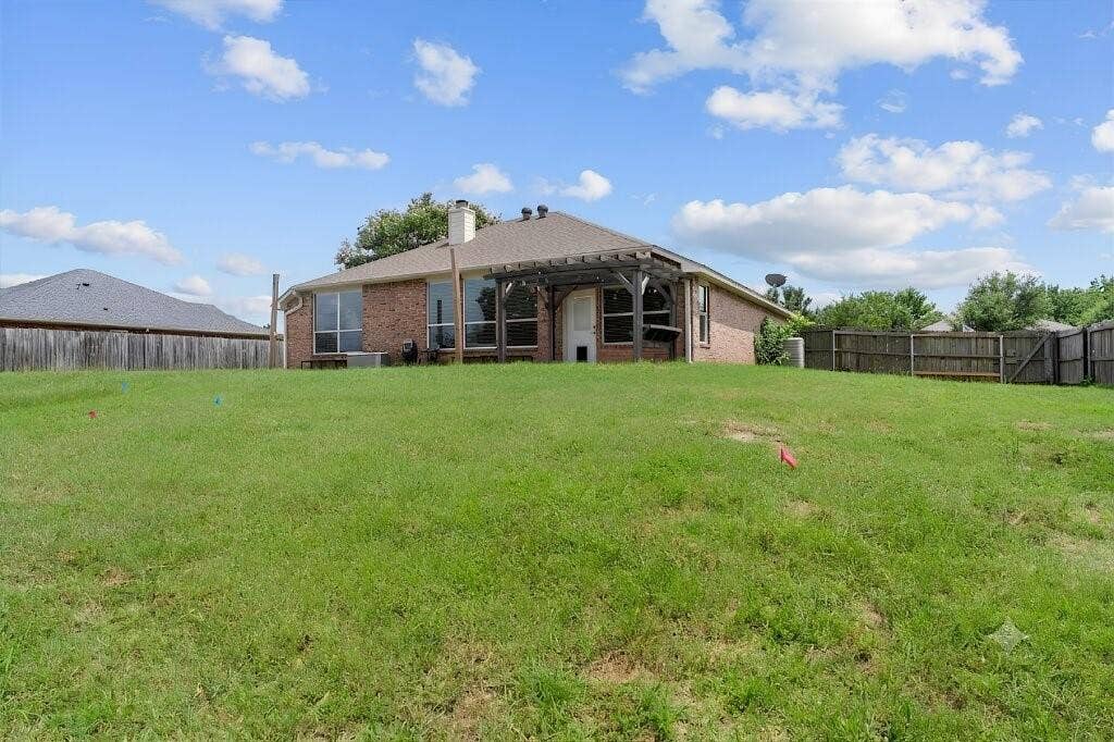 833 Greenwood Circle, Lindale, TX 75771 Expansive backyard featuring a manicured lawn, full perimeter wood fencing, and a brick exterior with a covered patio