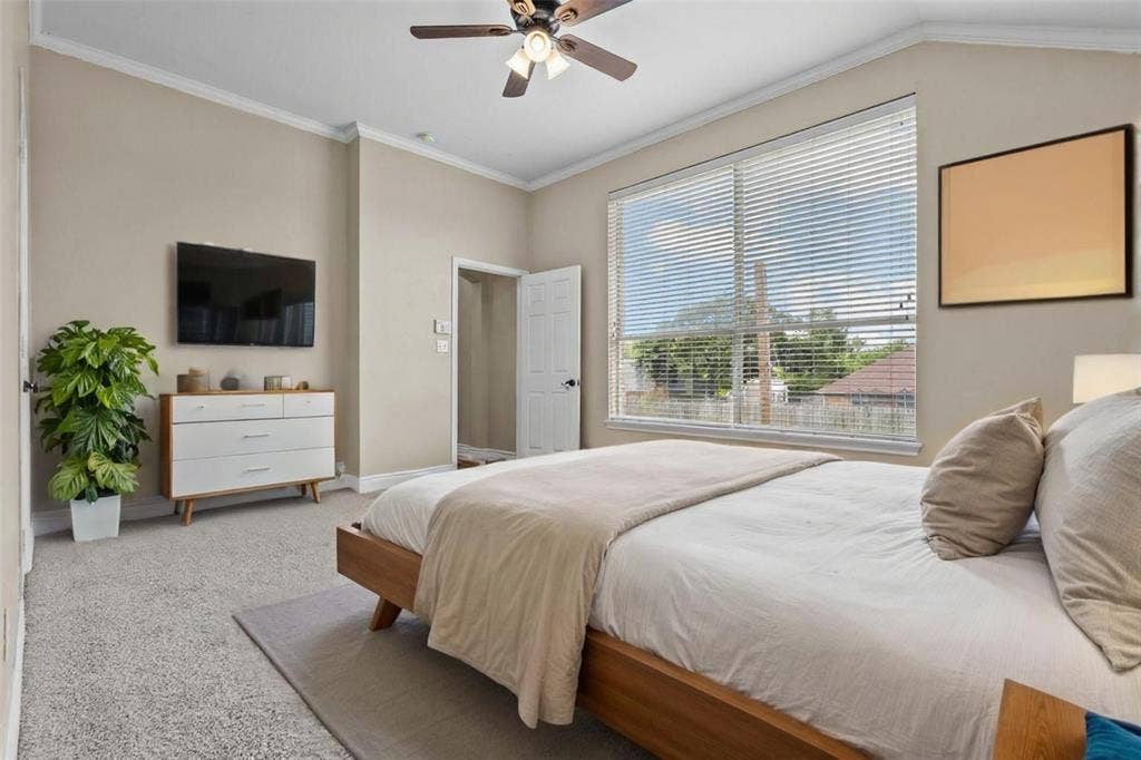 833 Greenwood Circle, Lindale, TX 75771 Spacious primary bedroom featuring a wood-finish platform bed, soft neutral palette, ceiling fan with integrated lighting, wall-mounted flat-screen television, built-in white cabinetry with decorative shelving, and expansive sliding glass doors with horizontal blinds opening to natural light and outdoor views