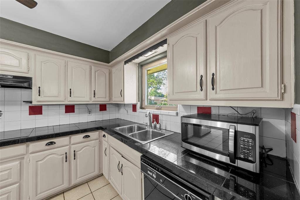 1116 Windsong Trail, Richardson, TX 75081 Cabinetry with arch panel doors, black countertop, dual basin stainless steel sink, and white tile backsplash with red accents