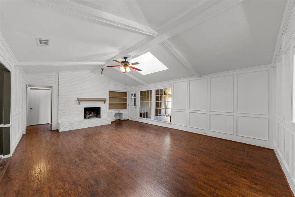 1116 Windsong Trail, Richardson, TX 75081 Vaulted ceilings with exposed beams, wood-finish flooring, white brick fireplace with mantel, built-in shelving, and skylight