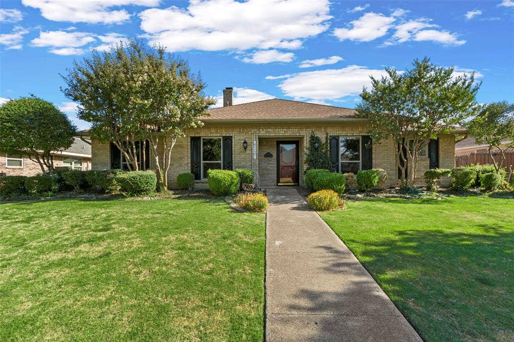 1116 Windsong Trail, Richardson, TX 75081 Single-story brick exterior with a traditional pitched roof, established landscaping, a concrete walkway, and dark window shutters
