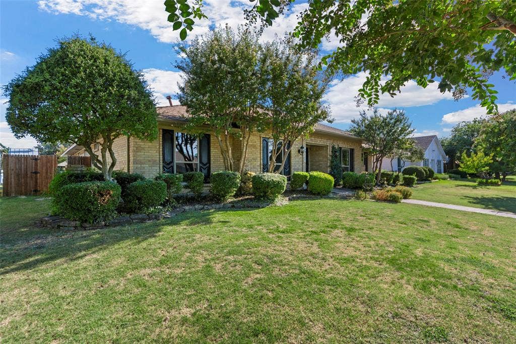1116 Windsong Trail, Richardson, TX 75081 Brick exterior with dark shutters, established landscaping, and a fenced side yard