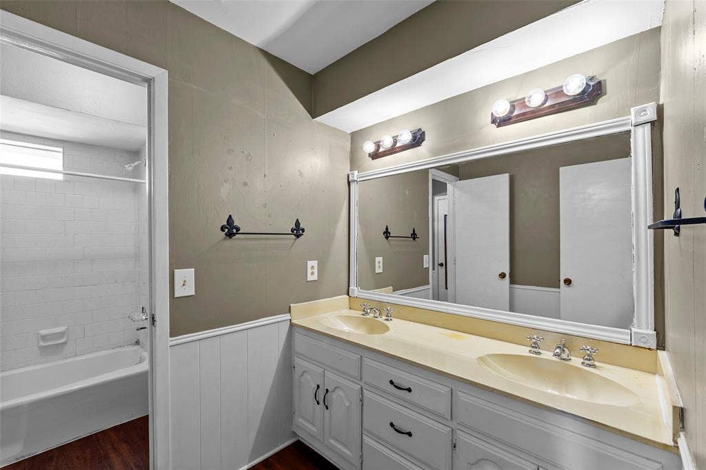 1116 Windsong Trail, Richardson, TX 75081 Dual vanity with integrated sinks and white cabinetry, large framed mirror, wood-finish flooring, and a tiled tub shower